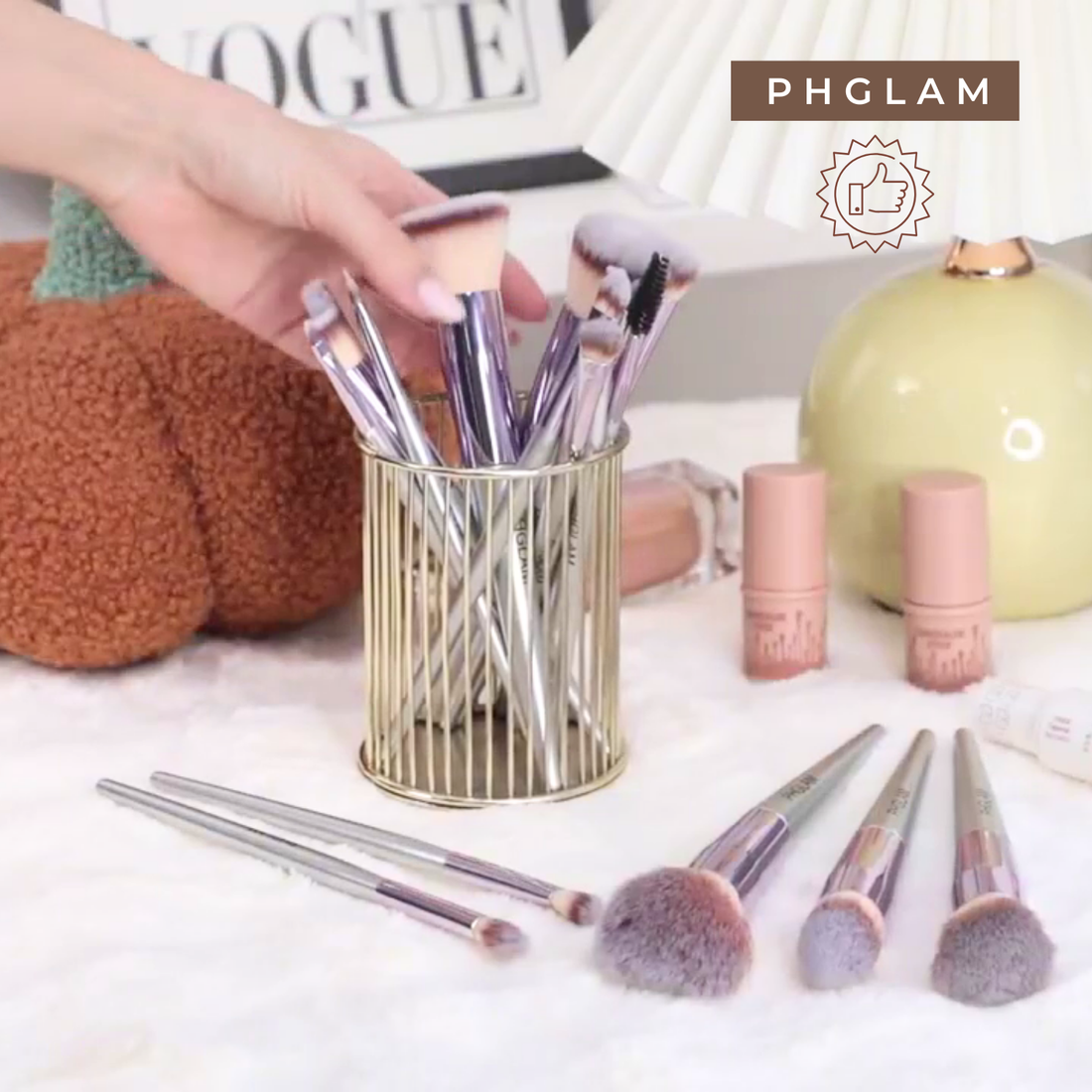 Makeup brushes in a holder with lip products on a table, featuring the PHGLAM brand.