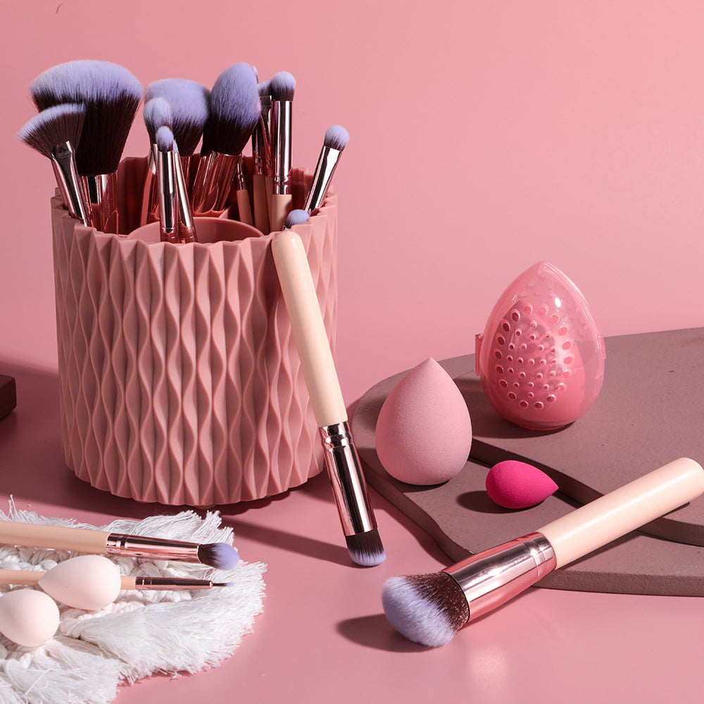 Makeup brushes and tools on a pink surface with a textured pink container.